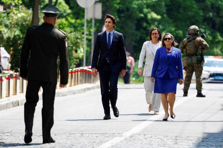 Prime Minister Justin Trudeau and Finance Minister Chrystia Freeland, who is wearing sunglasses, walk among heavy security on a sidewalk on their way to a memorial for Ukraine's war dead.