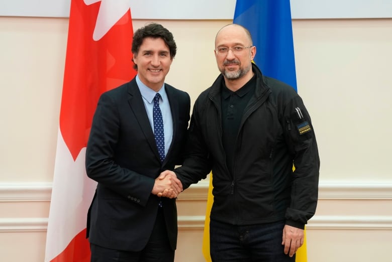 Canadian Prime Minister Justin Trudeau, in a suit, shakes the hand of a more casually dressed Ukrainian Prime Minister Denys Shmyhal in front of Canadian and Ukrainian flags.