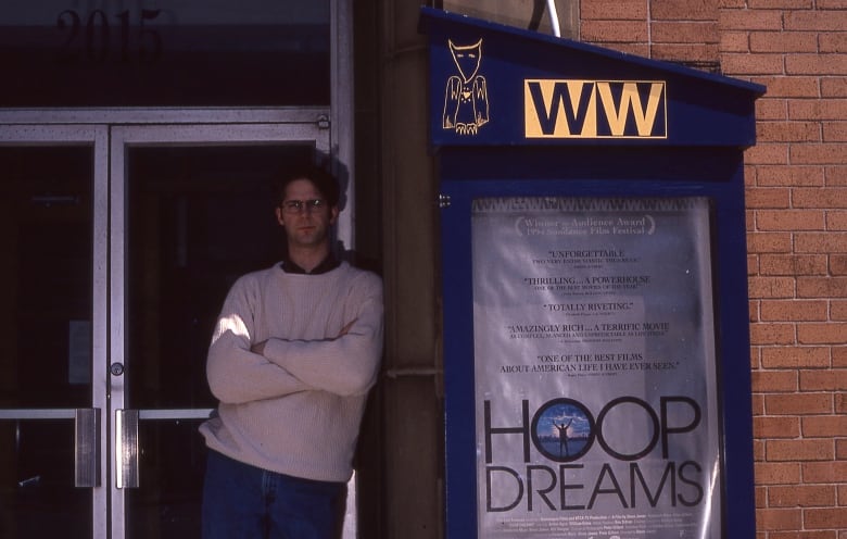 Peter Gaskin stands outside Wormwood's Dog and Monkey Cinema next to a poster for the documentary Hoop Dreams.