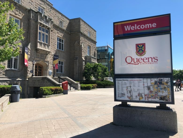 Exterior photo of a Queen's University sign with a campus building in the background