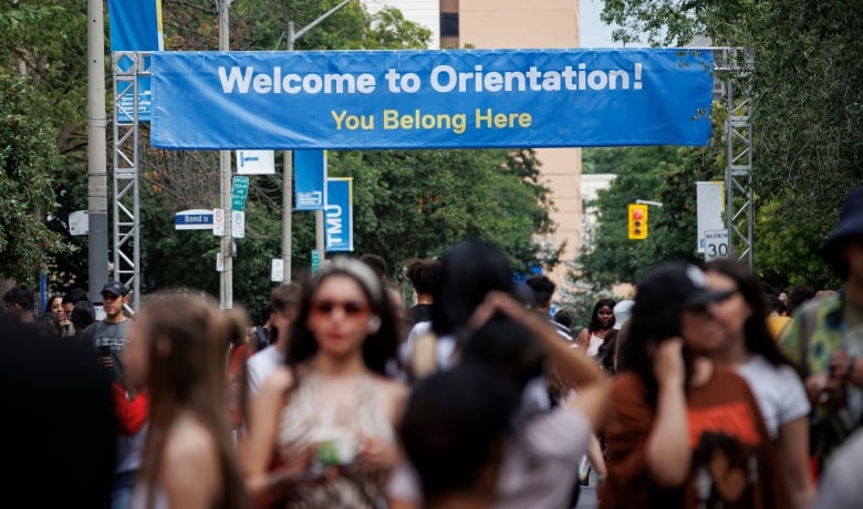 Students walking outdoors, photographed out-of-focus, below a banner that reads 'Welcome to Orientation! You Belong Here.'