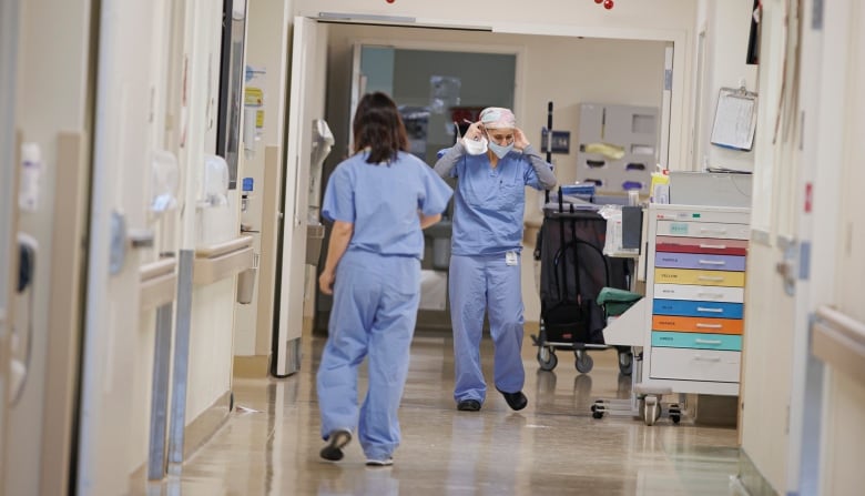 Two hospital workers wearing scrubs walk in a hospital hallway. 