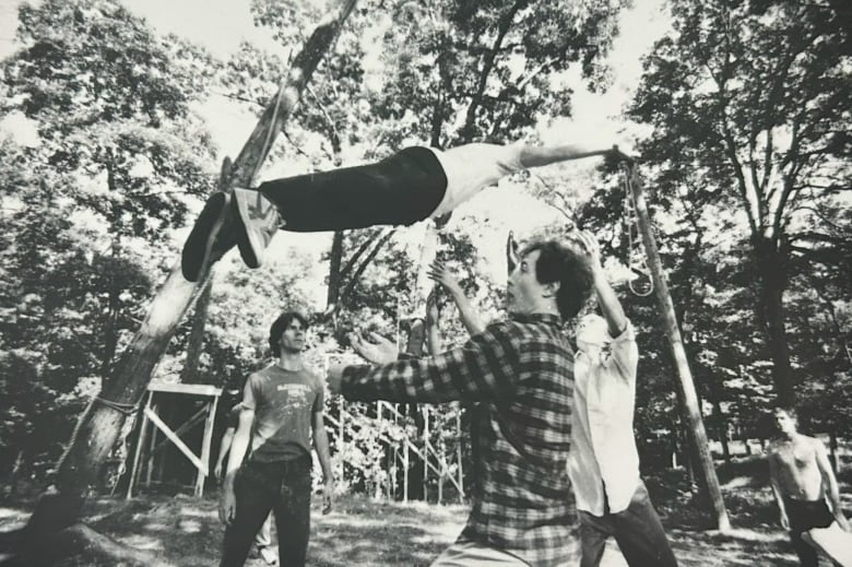 Black and white photo of three men toss another man into the air.