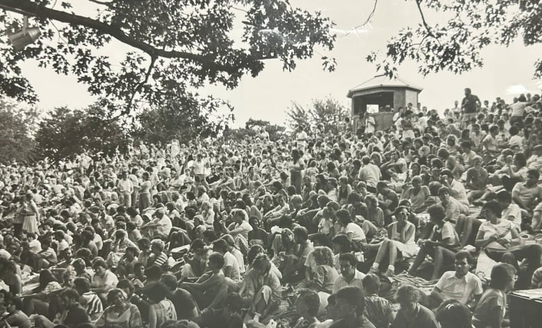 A black and white photo shows people sitting tightly packed on a hill.