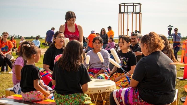 A group of children play an Indigenous drum.