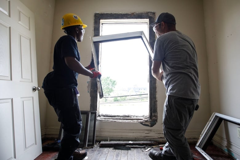 Tim Zubek, site supervisor with Building Up, and Dorine Khainza, an apprentice, are photographed pulling a window frame from the wall of a Toronto home under construction on July 6, 2023. 
