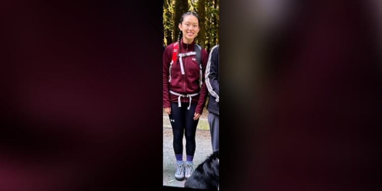 A teen girl is pictured in a maroon jacket, black leggings and hiking shoes, carrying a backpack.