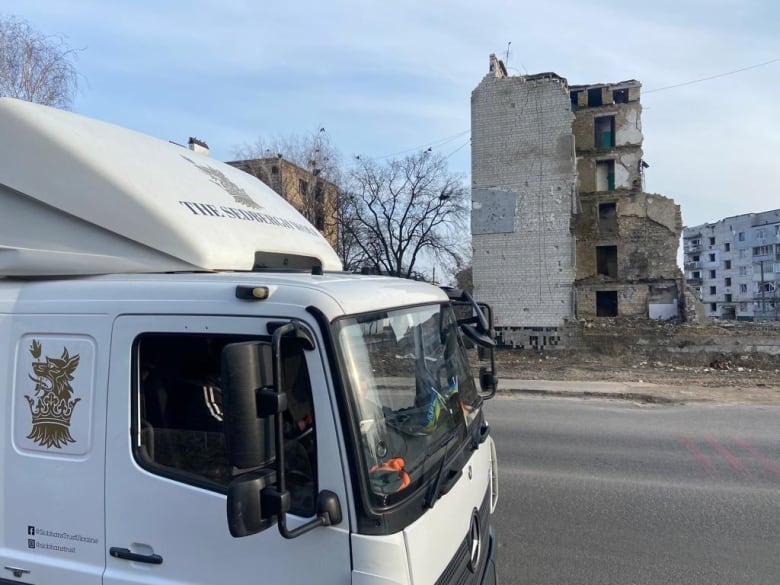 A truck passes by buildings that have been destroyed. 