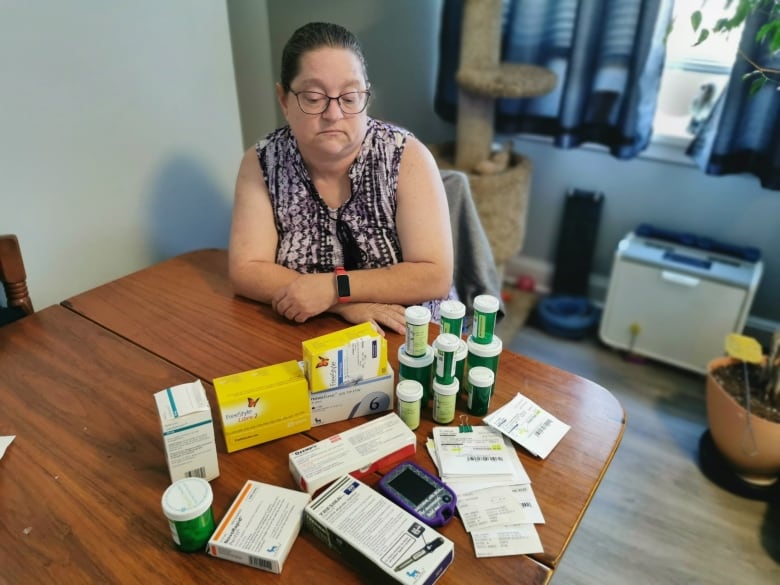 A woman sits at a table with various medications.