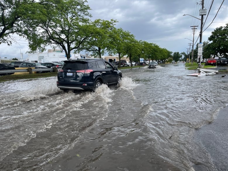 A black minivan drives down a street covered in water.