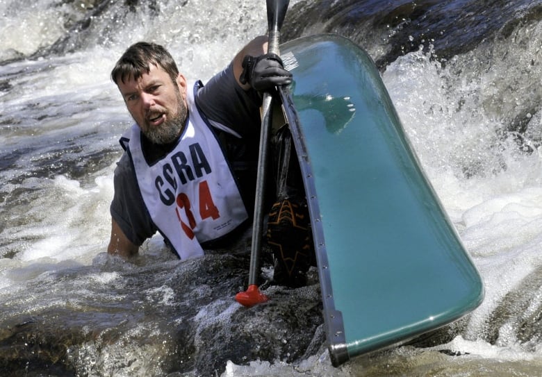 A man sits in a tipped over green canoe in river rapids