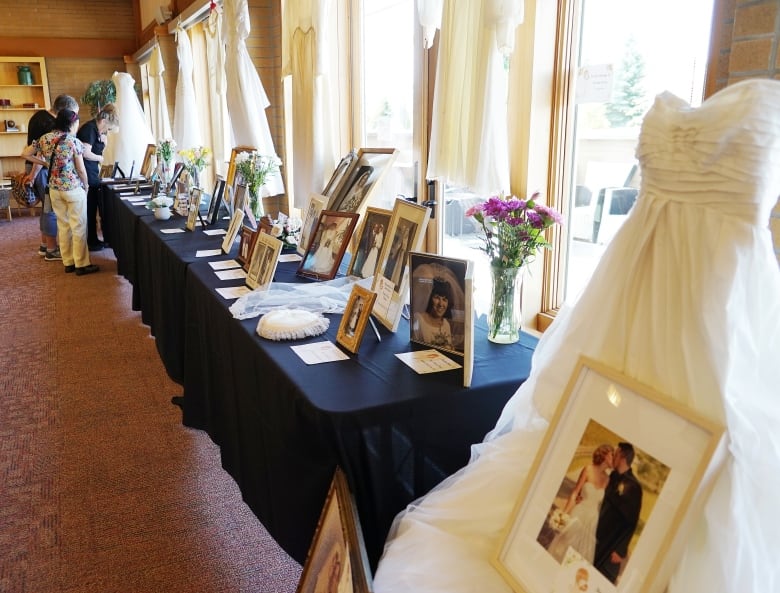 People look at table with wedding photos, wedding dresses are hanging beside or above table on display