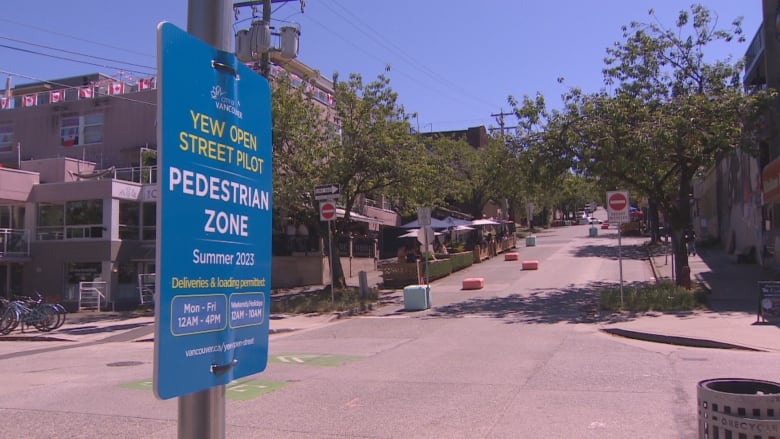 A blue sign in a street says "Yew Open Street Pilot. Pedestrian Zone."