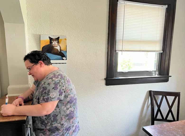 Jessica Mailloux-Lesperance writes a note in her kitchen, photo of her cat Spook in the background. 