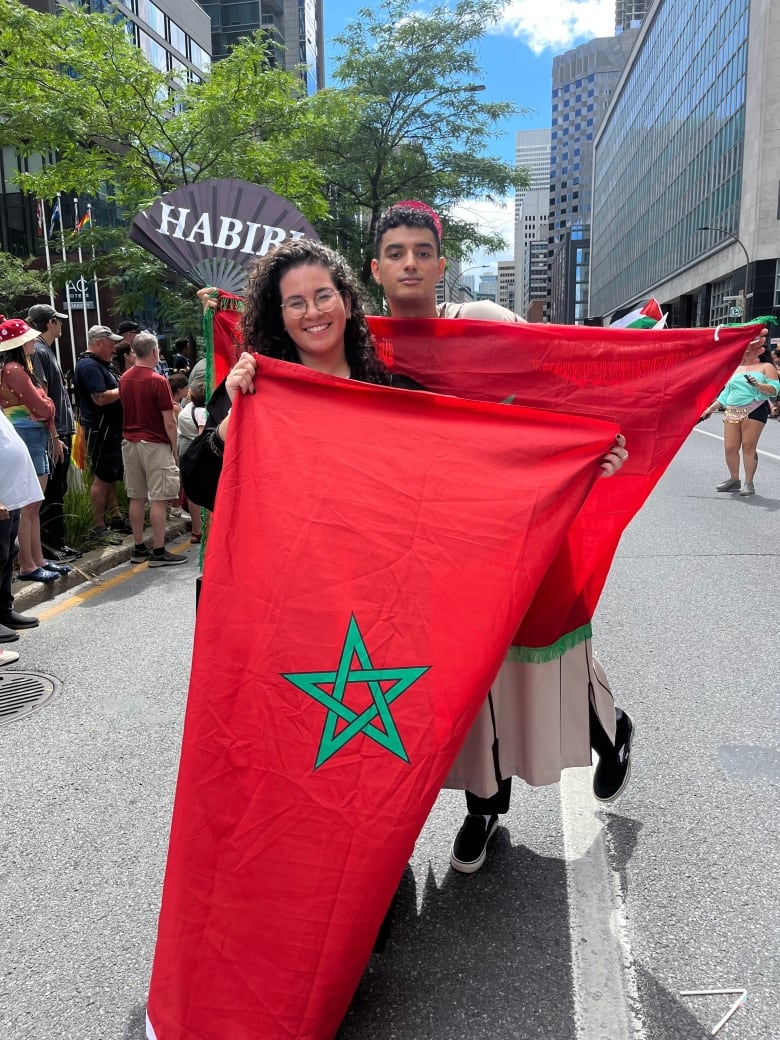 A woman and a man stand close to each other each one holding a Moroccan flag. 