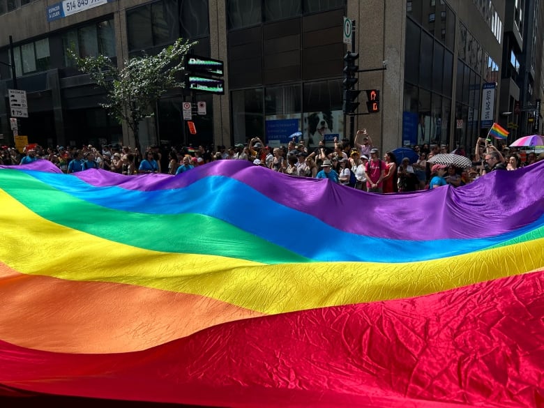 a huge pride flag fills most of the frame. It's being held by several people marching through the streets of Montreal during the Montreal pride parade. 