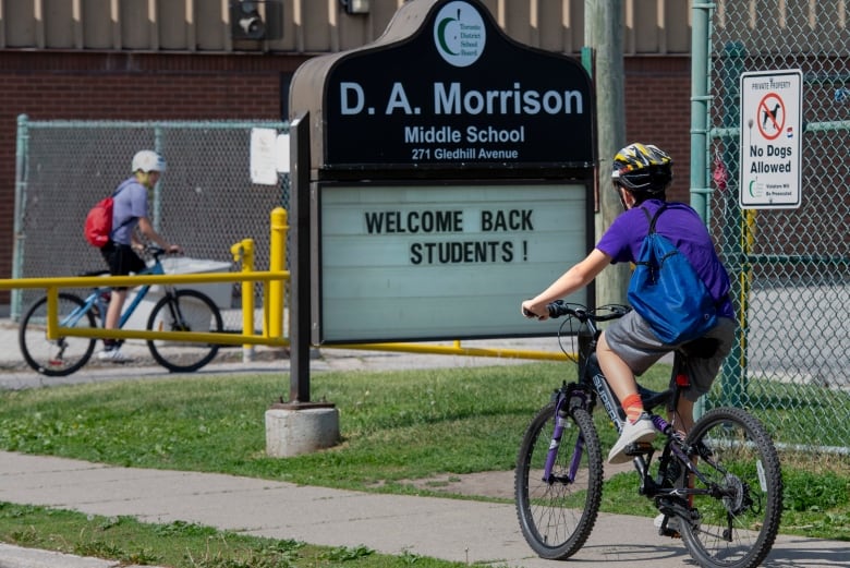 Two children ride their bikes past the sign for D.A. Morrison Middle School