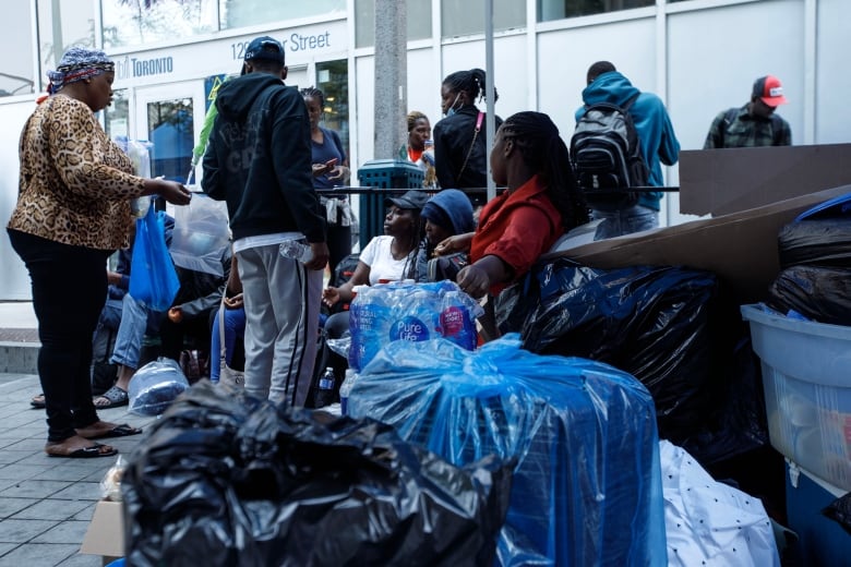 Luggages wrapped up in blue and black plastic bags with some people standing behind them. 