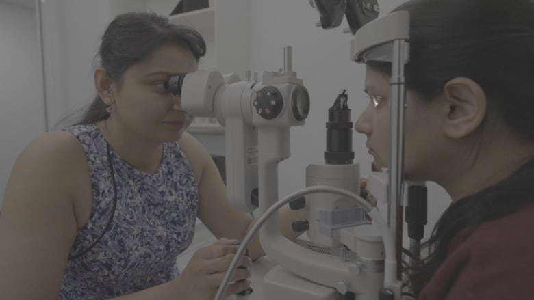 A woman uses a machine to examine another person's eye. 