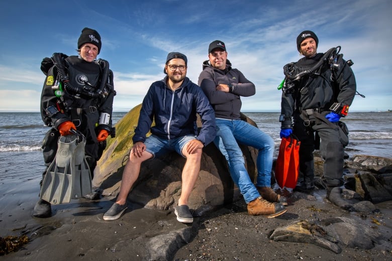 A group of divers take a group photo along a beach. 