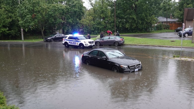 A car sits in a flooded street, with water midway up its wheels. 