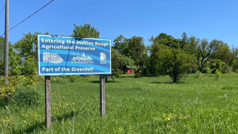 A sign on a grassy field indicates the entrance to the Duffins Rouge Agricultural Preserve. There are trees in the background.