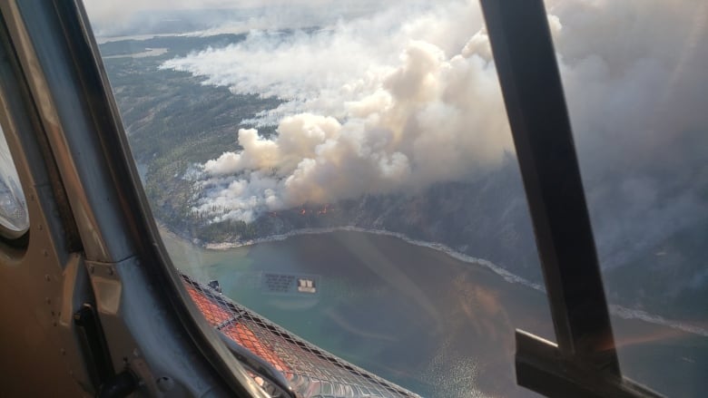 Looking out of an aircraft at a wildfire below, burning near a lake.