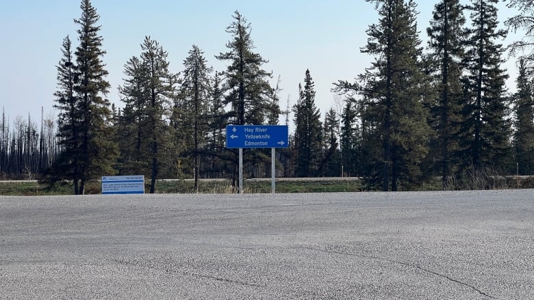 Picture of sign directing people to Hay River with burned trees in background.