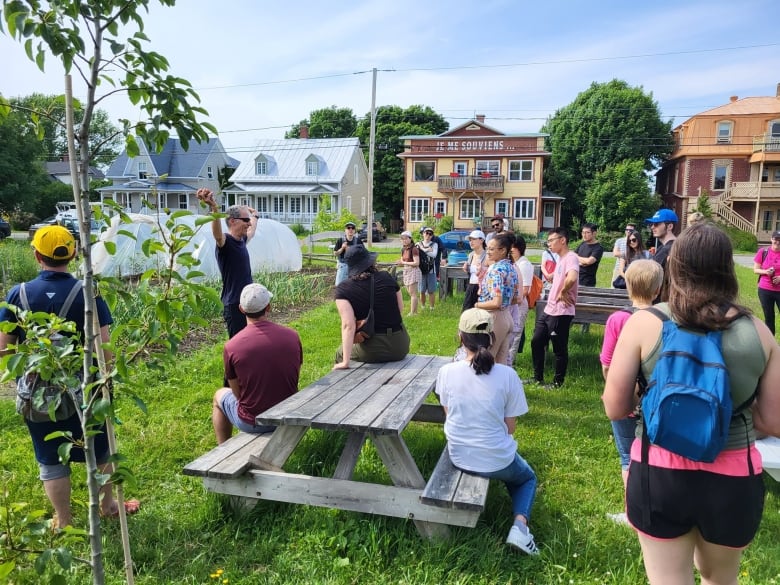 A group of students gather around picnic tables to watch a presenter in an urban agricultural environment.