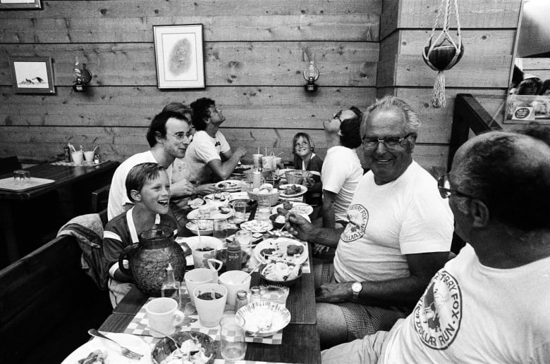Black and white photo of Terry Fox having a meal with people from the Canadian Cancer Society Team. 