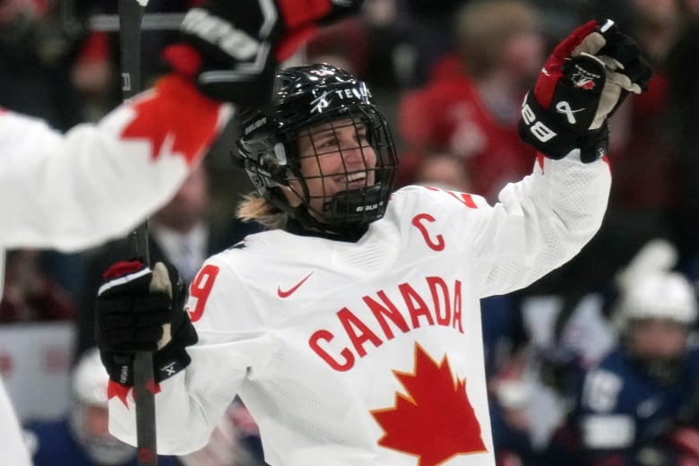 A hockey player lifts up her arms in celebration.
