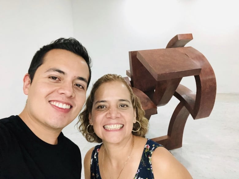 Two people smile as they take a selfie in front of a wooden sculpture. 