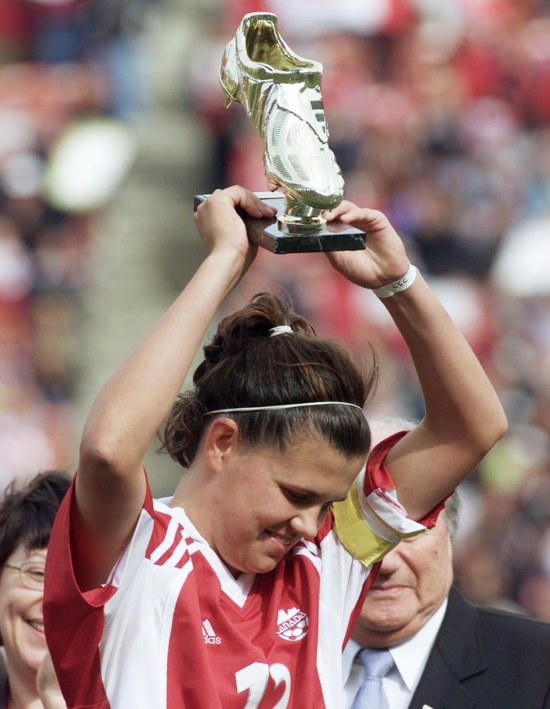 A woman soccer player holds a trophy above head.