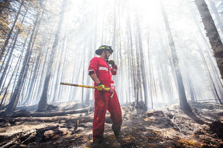 A man in a red jumpsuit stands in the woods with an axe in the hands.