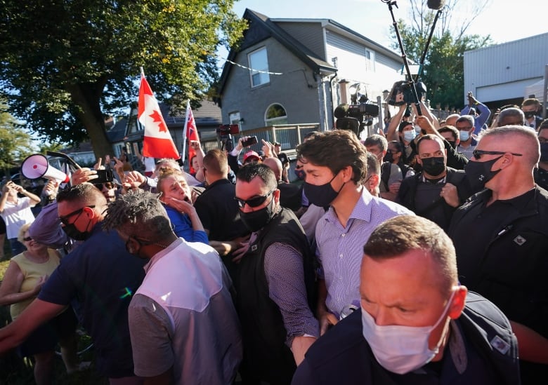 Liberal Leader Justin Trudeau is escorted by his RCMP security detail as protesters shout and throw rocks while leaving a campaign stop at a local micro brewery during the Canadian federal election campaign in London Ont., on Monday, September 6, 2021. 