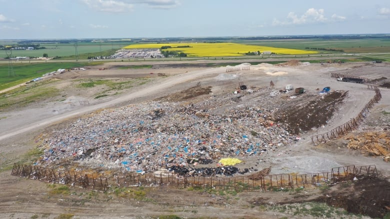 A view from above of garbage in a landfill in summer, with a yellow canola field in the background