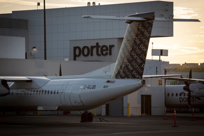 A small Porter aircraft is parked in front of Billy Bishop Airport at dusk. 