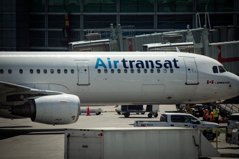 An large aircraft with the words Air Transat on the side is parked on a tarmac. 
