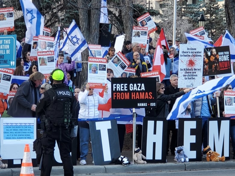 Protesters stand on the side of a city street, holding Israeli flags and signs.