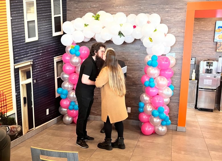 A couple kiss underneath a decoration of balloons.