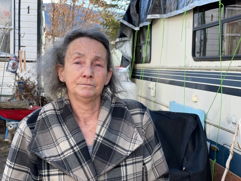 A woman outside a trailer looks at the camera.