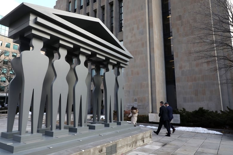 A sculpture of people making up columns under a roof sits outside a courthouse. 