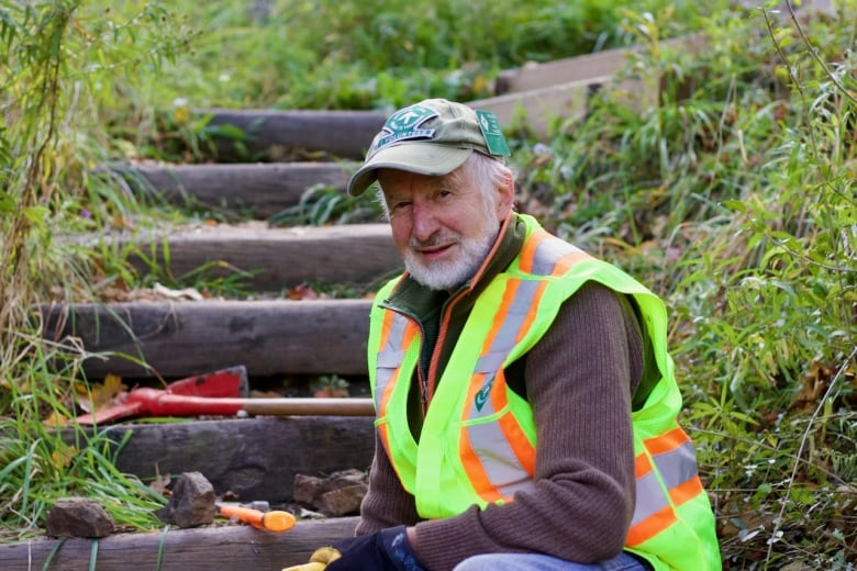 A portrait of a person in a safety vest sitting on steps outdoors. 