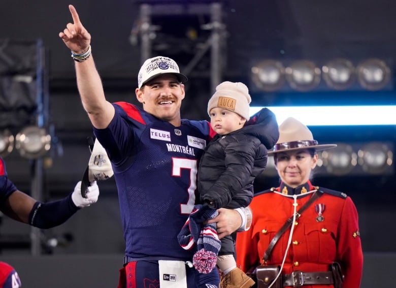 A football player points in the air while holding his son.