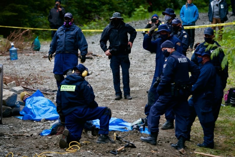 RCMP officers surround a protester cemented into the ground during a protest in Fairy Creek using a technique called a Sleeping Dragon