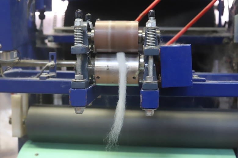A piece of spun wool comes out of a machine between two wheels.