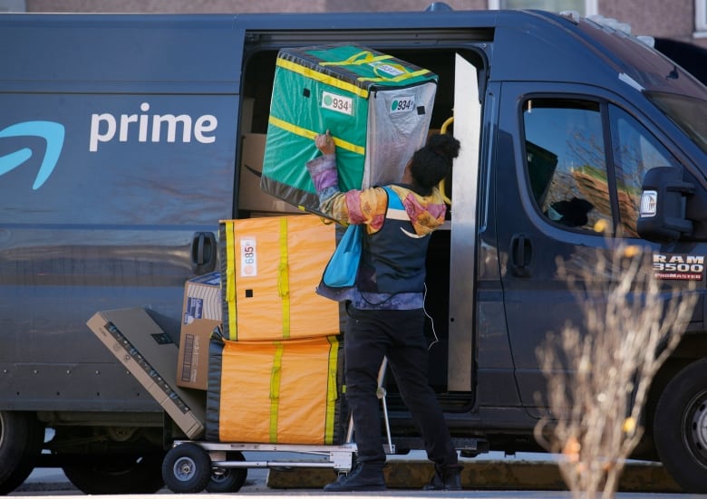 A worker in black-and-blue vest lifts a large package out of an Amazon delivery truck.