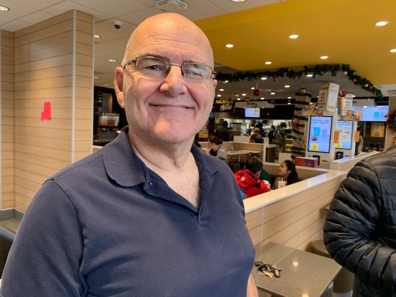 A bald man in a navy polo stands in a McDonald's, smiling at the camera. 