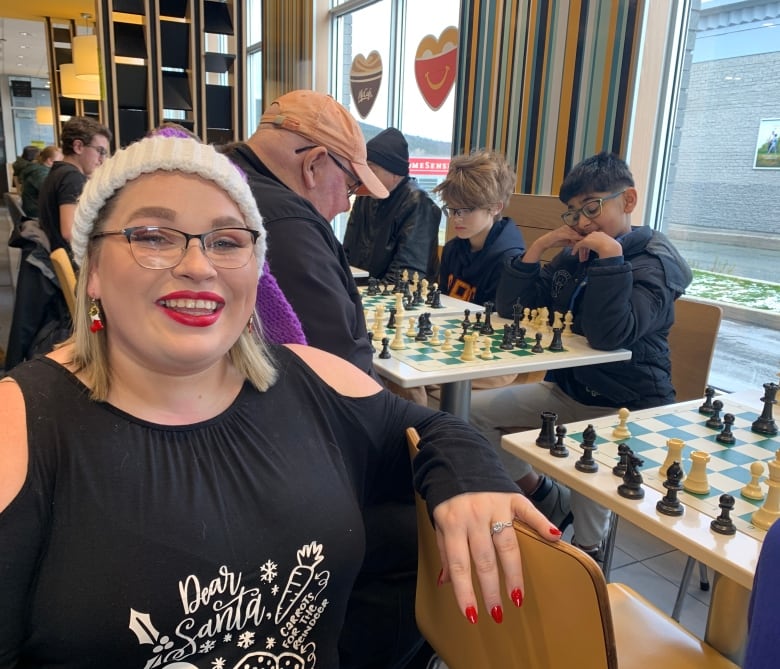 a woman in a black shirt and a santa hat sits with chess games behind her. 