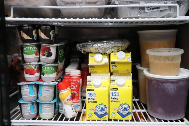The inside of a fridge displaying a shelf of yogurt, cream and plastic containers. 
